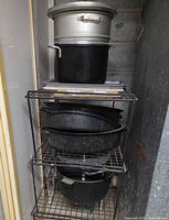 tower of cookware showing aluminum stock pot, black stock pot, two speckled enamel roasters with lids, and baking sheet