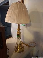 Full view of brass table lamp with pleated shade wrapped in plastic