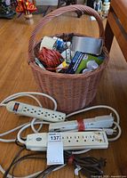 Overall lot showing basket with tapes, twine, hooks, glue, two surge protectors and fluorescent light fixture