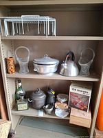 Overall view of shelf containing tea kettle, glass baskets, ice bucket, tiki mug, ice shaver box, coffee pot, bottle, wire racks