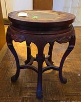 Full view of round carved wood side table showing legs and apron