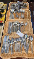 Four placemats filled with assorted stainless flatware showing overall quantity and pattern