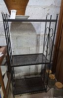 Full view of the black metal baker's rack showing three shelves and decorative sides