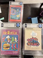 Close view of three slabbed games showing labels: BurgerTime graded 9.4, Bomb Squad graded 9.2, Night Stalker graded 8.0