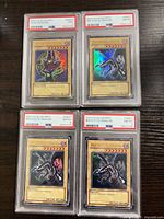 Four PSA-slabbed Yu-Gi-Oh cards laid out on table