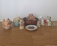 All eight cat figurines and dish grouped on surface