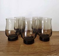 Five smokey brown glass goblets grouped on wood surface