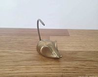 Left side view of brass mouse figurine showing body and tail spike