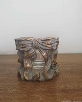 Front view of ornate grey and gold bow votive holder with glass insert inside