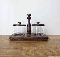 Front view showing two glass jars with wooden lids on wooden tray