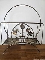 Full front view of brass magazine rack showing circular handle and maple leaf motif