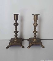 Front view of both brass candlesticks showing square bases and feet