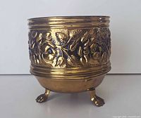 Front view of brass planter showing rose embossing and claw feet