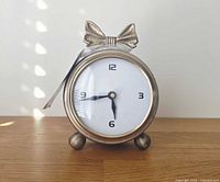 Front view of antique gold resin desk clock with bow accent and white face