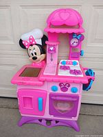Front view of entire Minnie Mouse play kitchen showing colors, Minnie figure, stovetop, oven and refrigerator doors