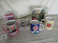 Group shot of all six items: four mugs, alarm clock, sealed Barbie doll set