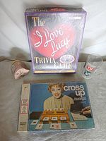 Group shot of all four items: two game boxes, tin, glass