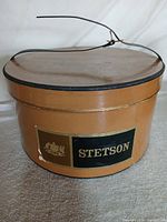 Tan round Stetson hat box front view showing label and strap wire