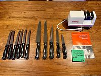 All twelve knives, Chef'sChoice Diamond Hone sharpener, power cord, and instruction booklet laid out on wooden surface