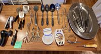 All 24 kitchen utensils laid out showing variety: prep tools, turners, spoons, ladle, tongs, whisks and skewers plus stainless bowl holding whisks/skewers