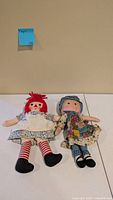 Raggedy Ann and Holly Hobbie cloth dolls on table displaying full outfits and size comparison