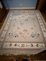 Full view of 5' x 8' pink and cream floral wool area rug showing pattern, colors, stains, and fringe wear