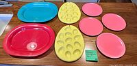 all eight plastic pieces laid out: turquoise platter, red platter, two yellow deviled egg trays, four pink plates