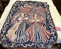 Full view of the tapestry throw blanket showing angel motif, colors, and fringe