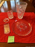 Vase, platter, covered candy dish (base and lid) and butter tray arranged on red cloth