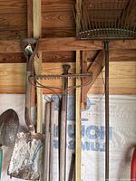 Group of shovels and metal tine rake hanging on wall