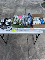 Overall view of table with reflector lamp, packaged CFL and LED bulbs, loose and boxed fluorescent tubes, loose reflector bulbs