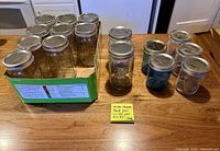 All mason jars grouped: 12 clear quart jars in cardboard box, 4 clear pint jars and 4 blue half-pint jars on countertop, all with silver screw lids