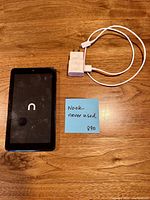 Front view of Nook e-reader with boot logo, USB cable, and wall charger on tabletop