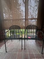 Front view of two black metal mesh patio armchairs on tiled porch floor
