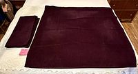 Two burgundy corduroy square tablecloths, one unfolded, one folded