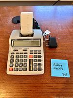 Casio HR-100TM printing calculator with paper roll and AC adapter on wooden surface