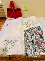 Tablecloth, four dish towels and Santa legs wine carrier displayed on table