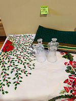 Tablecloth holly print, stacked green placemats, two clear glass angel candle holders