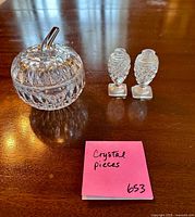 Apple-shaped lidded crystal bowl and two footed crystal shaker bodies on wood surface