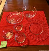 All six clear glass pieces displayed on red cloth: two plates, three footed bowls, one pedestal compote