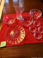 All eight clear glass pieces laid out on red cloth: pitcher, charger plate, two large bowls, four small bowls