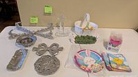 All items laid out showing ceramic basket, rabbit planter, six silver-tone trivets/trays, glass cross, paper plates, napkins and cupcake liners
