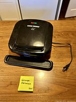 Closed George Foreman grill with power cord and drip tray shown