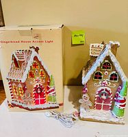 Gingerbread house accent light standing beside its original box, power cord and replacement bulbs visible