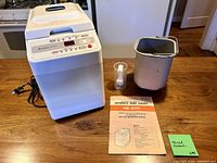 Bread maker front view with bread pan, scoop and manual