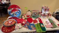Overview of holiday trays, cups, napkins, towels, mitts, potholders, cookie cutters and ornaments displayed on table