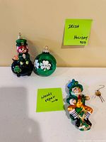 Three Irish-themed glass ornaments displayed on table with notes indicating repair needed