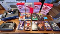Overall lot showing JVC VCR with remote and cables, VHS rewinder, twelve VHS tapes and four popcorn boxes