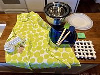 All items laid on countertop: apron, bowls, measuring cups, baking dish, spatulas, lids, trivet