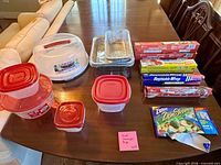 All items arranged on table: cake carrier, containers, pans, boxed wraps, and bags